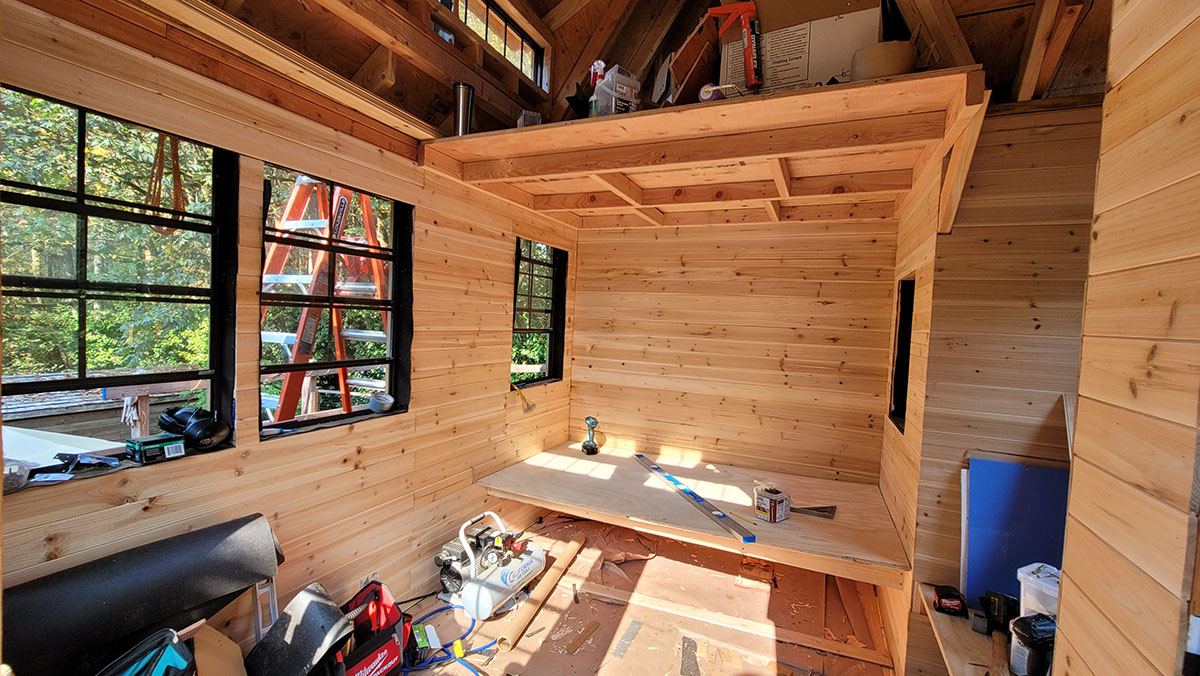 The cedar-lined interior of a treehouse under construction, with tools and a ladder